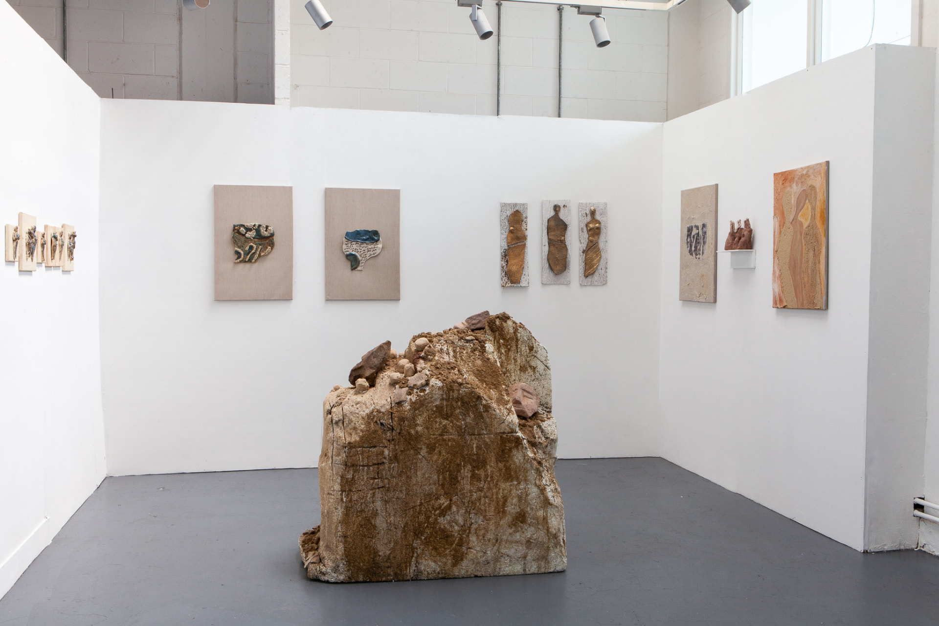 Gallery installation view with a large central earthen sculpture and wall works