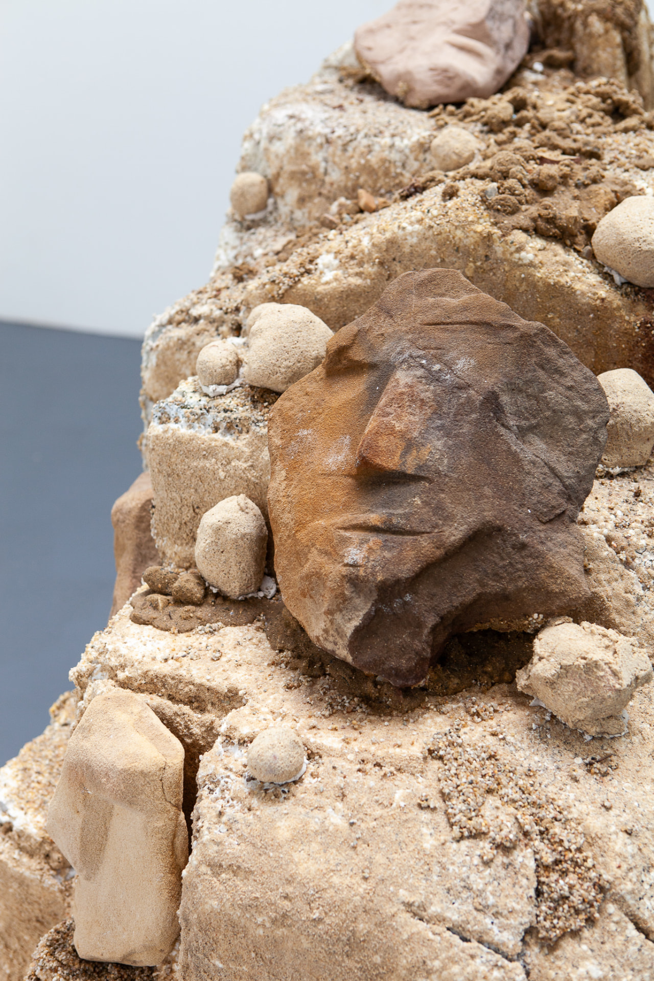 Detail of a weathered brown face fragment emerging from a sandy form