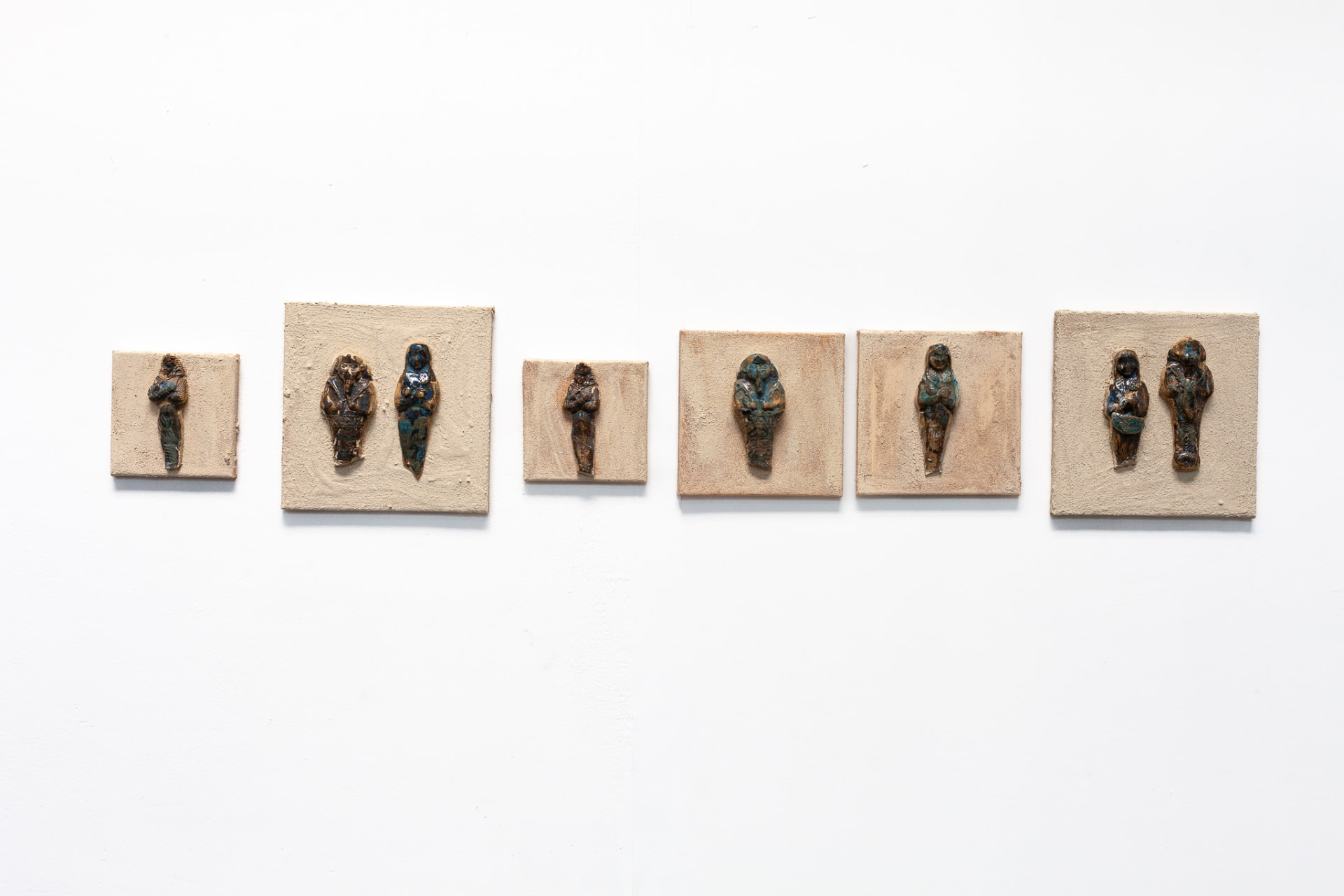 Wall-mounted installation of small glazed ceramic figures on square panels