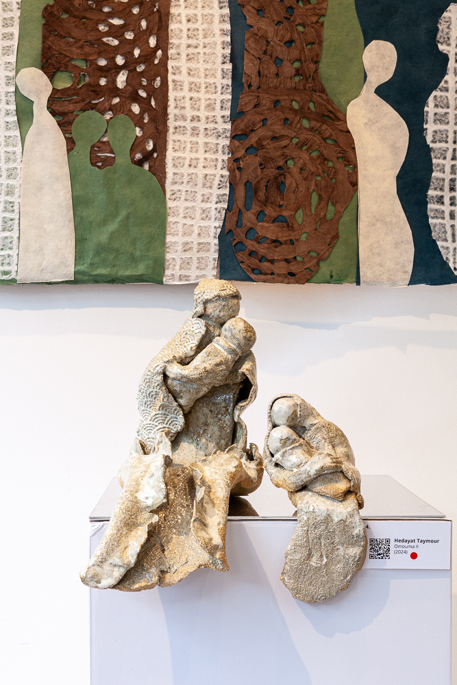 Ceramic sculpture of embracing figures in front of a collage