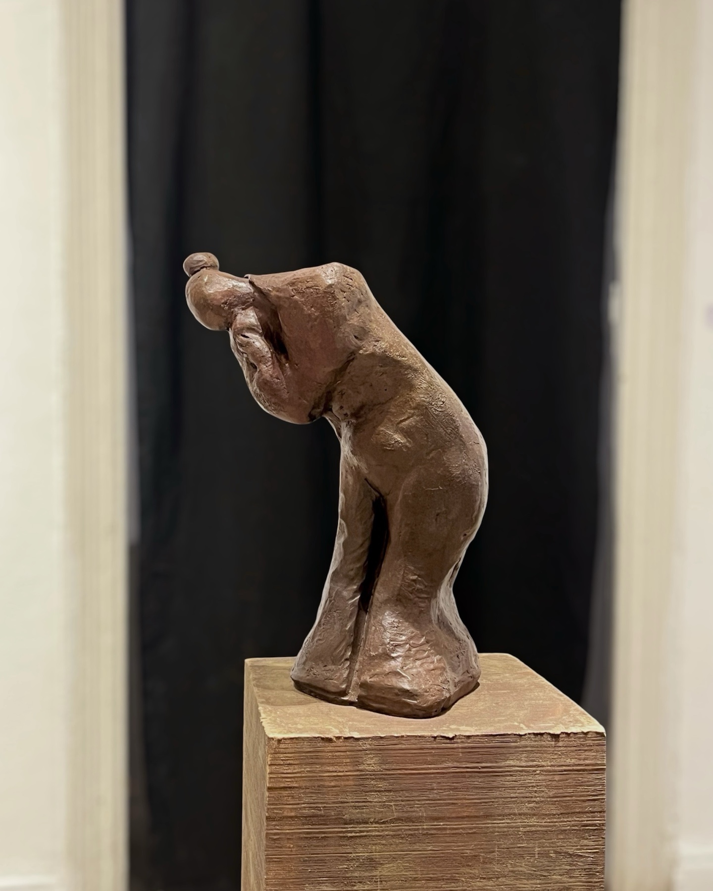 Single bronze bending figure on a wooden plinth