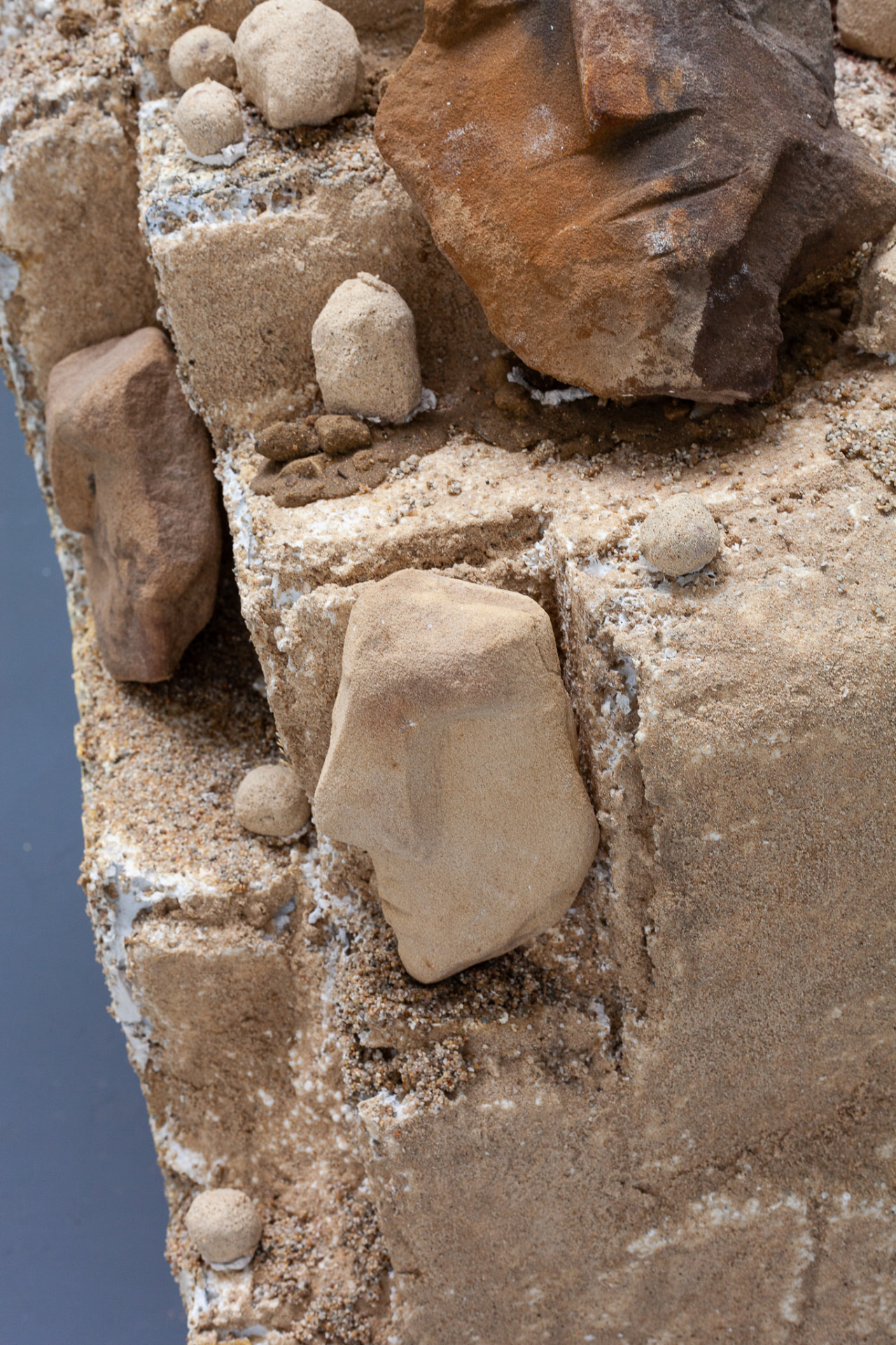 Detail of a sandy sculptural surface with embedded stone and ceramic forms