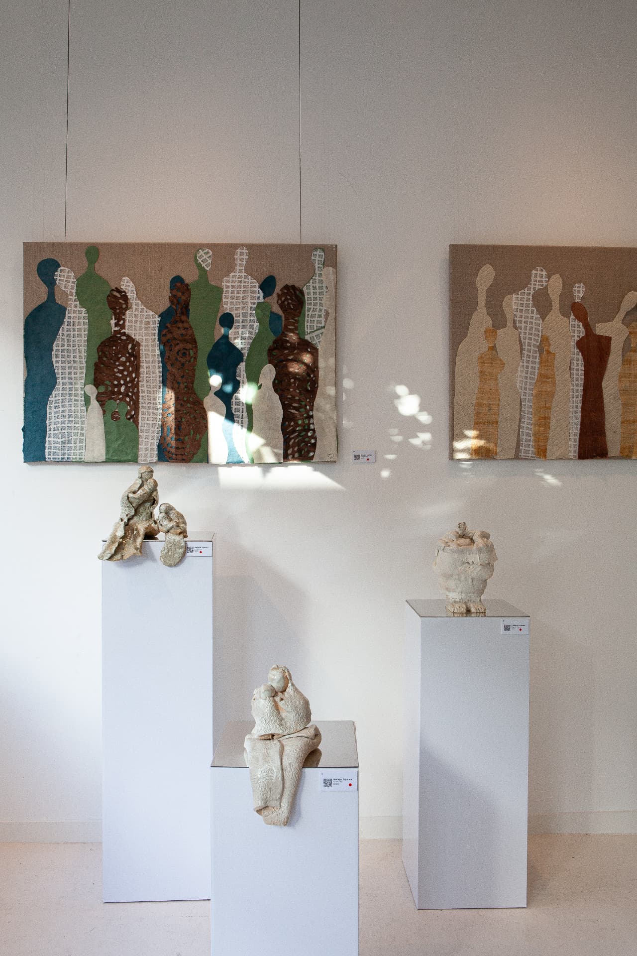 Installation view of collages and sculptures on white plinths